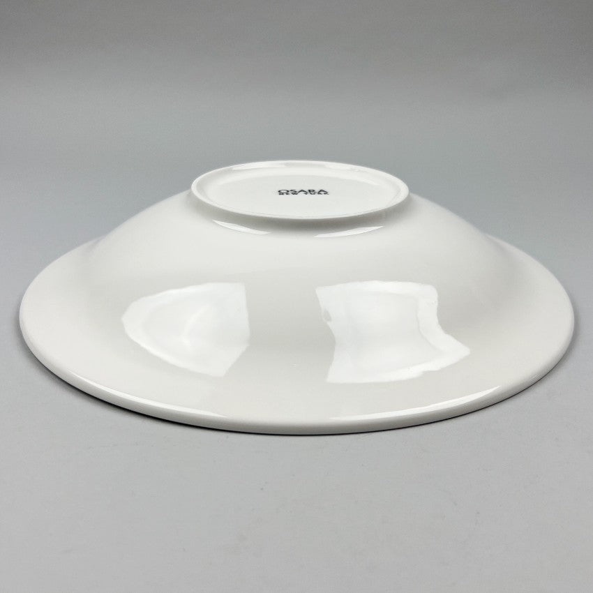 White ceramic shallow bowl with a deep pasta plate on a gray background, shot from the bottom angle.